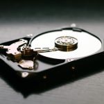 An open hard drive is displayed on a wooden surface, showcasing its internal components and metallic details.