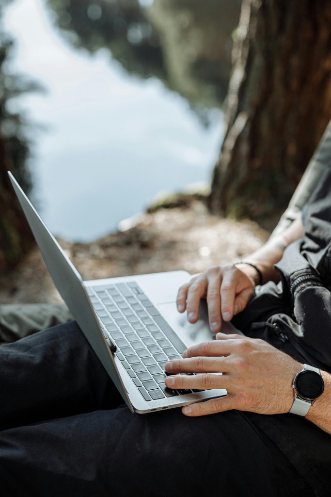 pexels-photo-5052293-5052293 An individual working on a laptop outdoors by a scenic lakeside, enjoying nature and technology together.